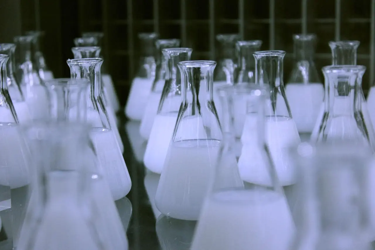 Glass laboratory flasks and measuring cylinders used for material testing.