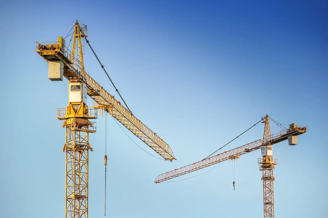 Two tower cranes standing above a concrete building under construction.